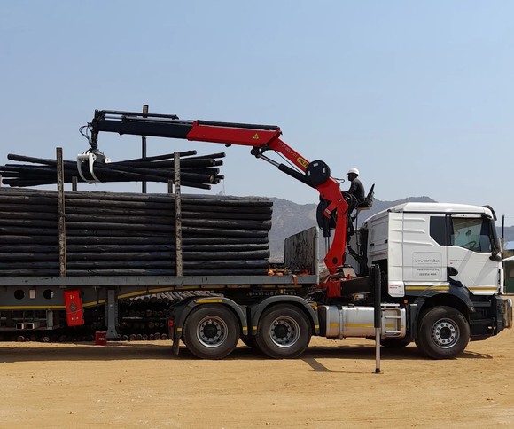 Two trailers loaded with treated wooden poles on red earth
